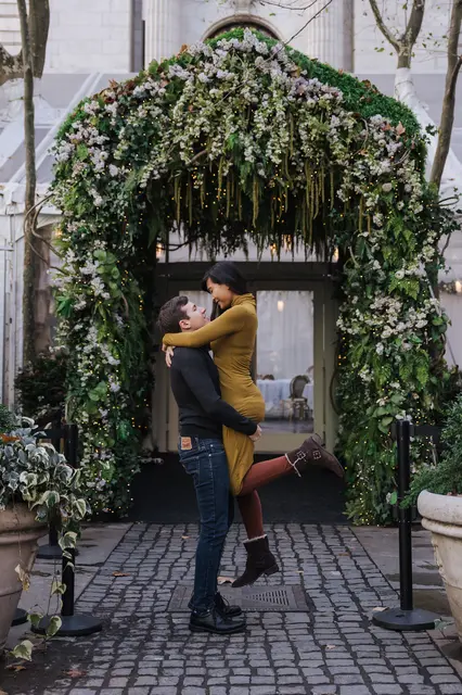ggraph of Chris and Emily in a doorway. Chris is holding Emily aloft, and she is looking down and smiling at him.